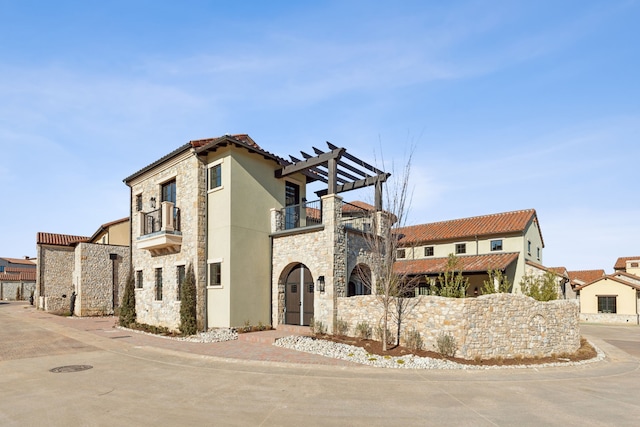 mediterranean / spanish-style home with stone siding, stucco siding, a balcony, and a pergola