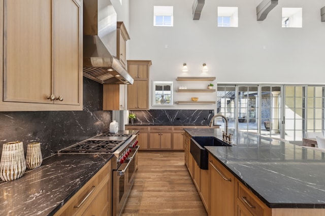 kitchen featuring range with two ovens, a sink, wall chimney range hood, a large island, and open shelves