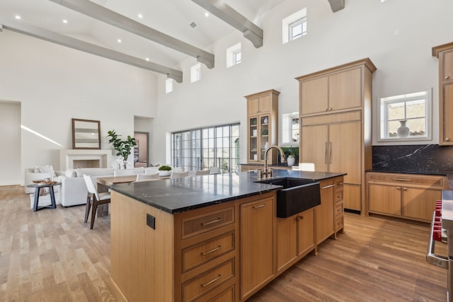 kitchen with open floor plan, a kitchen island with sink, a sink, dark stone counters, and beamed ceiling