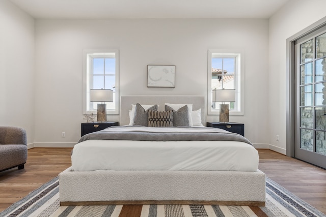 bedroom with access to outside, multiple windows, baseboards, and wood finished floors