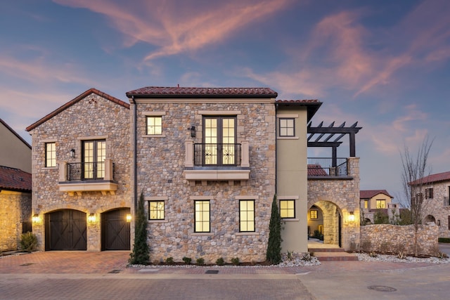 view of front of home featuring a balcony, a pergola, stone siding, a tile roof, and decorative driveway