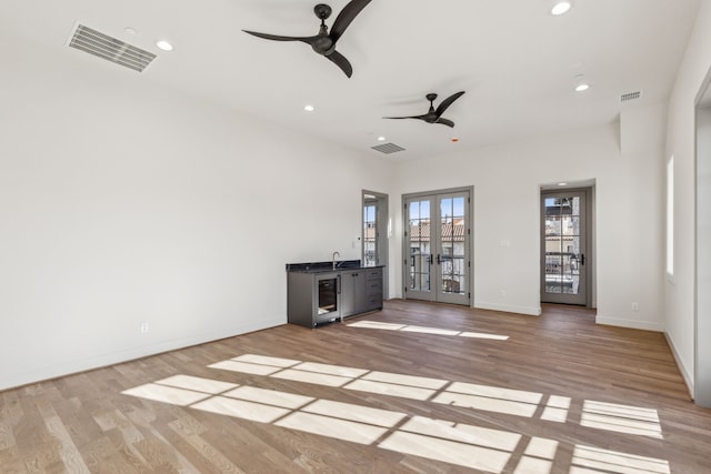 unfurnished living room featuring light wood-style floors, visible vents, a ceiling fan, and french doors