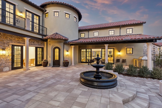 back of property featuring a tile roof, stucco siding, french doors, a balcony, and stone siding