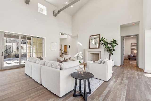 living area with stairway, light wood-style floors, high vaulted ceiling, beamed ceiling, and baseboards