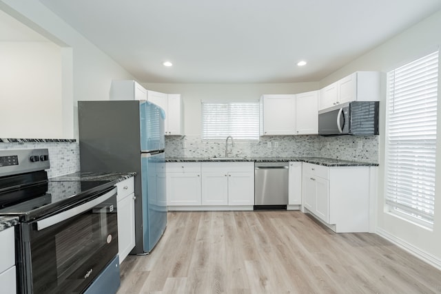 kitchen featuring stainless steel appliances, a sink, white cabinetry, light wood-style floors, and dark stone counters