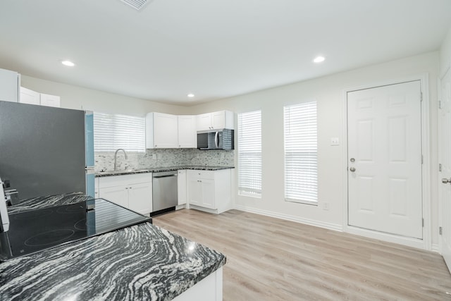 kitchen with white cabinets, light wood-style flooring, appliances with stainless steel finishes, dark stone countertops, and a sink