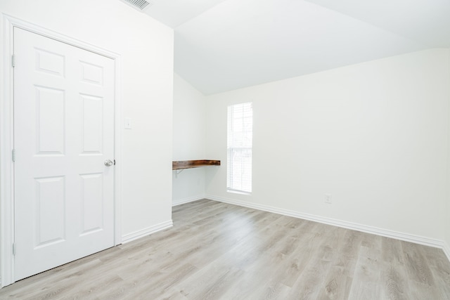 empty room with light wood-style flooring, baseboards, and vaulted ceiling