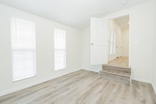 spare room with lofted ceiling, baseboards, and light wood finished floors