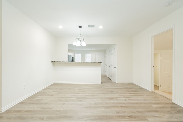 unfurnished living room with baseboards, light wood finished floors, and a notable chandelier