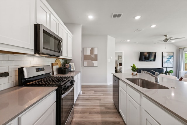 kitchen with a sink, visible vents, white cabinetry, open floor plan, and appliances with stainless steel finishes