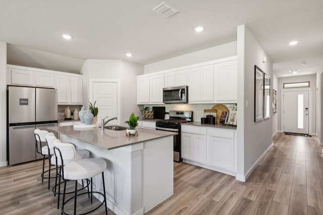 kitchen with a center island with sink, white cabinets, stainless steel appliances, light wood-style floors, and a sink