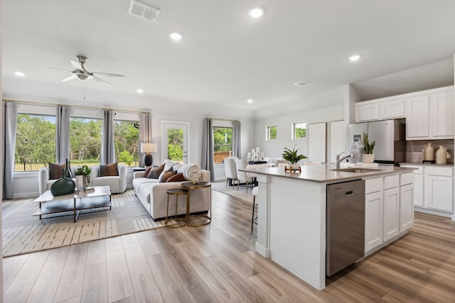 kitchen with light countertops, appliances with stainless steel finishes, a kitchen island with sink, white cabinets, and a sink