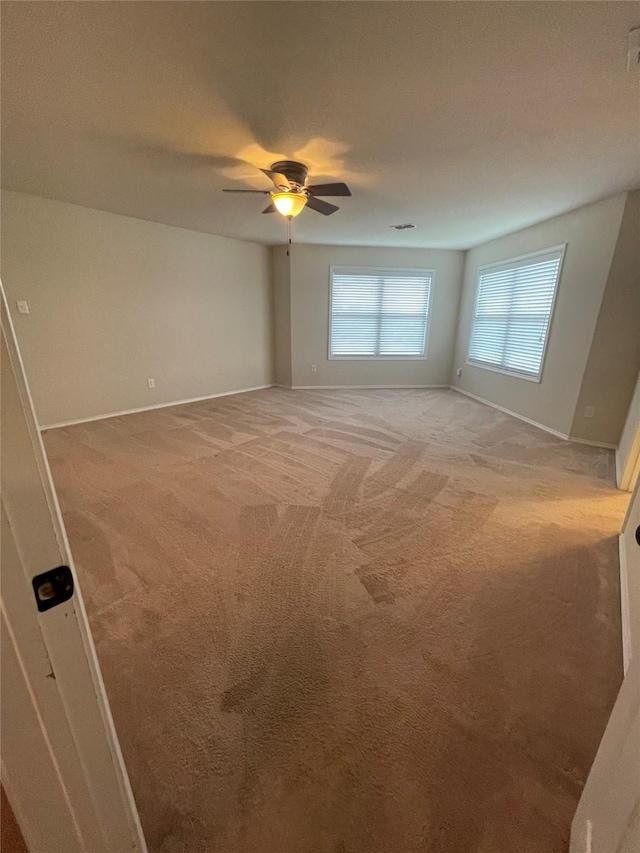 carpeted spare room with a ceiling fan and baseboards