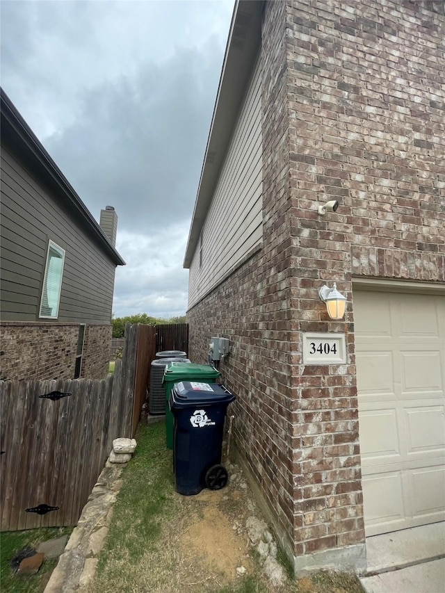 view of home's exterior with an attached garage, fence, cooling unit, and brick siding