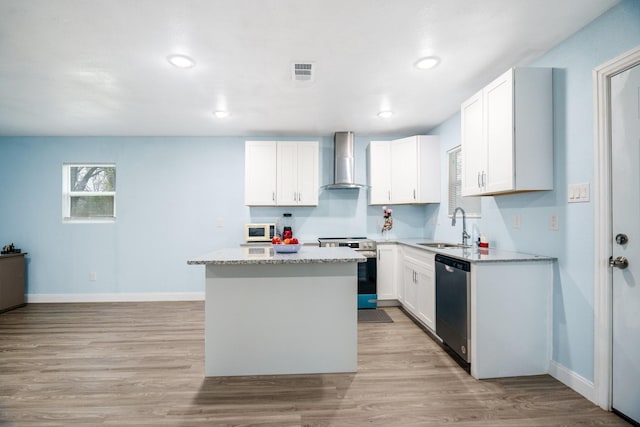 kitchen featuring stainless steel appliances, a sink, a kitchen island, white cabinets, and wall chimney exhaust hood