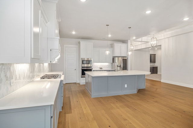 kitchen with light countertops, an island with sink, white cabinets, and stainless steel appliances