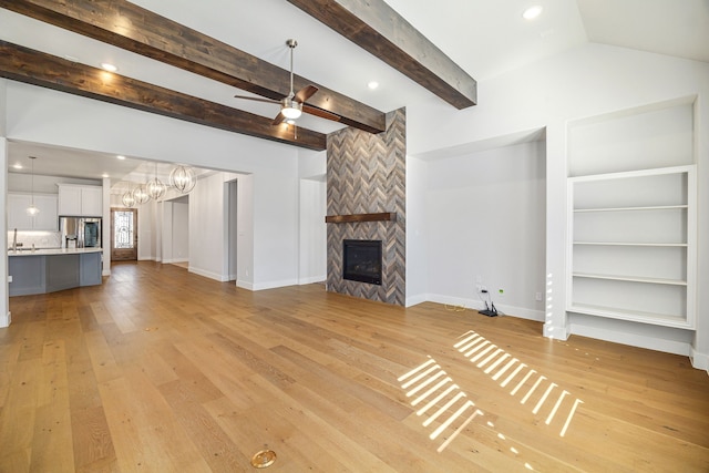 unfurnished living room featuring light wood-type flooring, a large fireplace, baseboards, and ceiling fan with notable chandelier