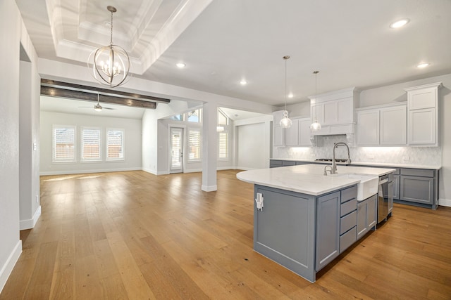 kitchen with tasteful backsplash, open floor plan, hanging light fixtures, a kitchen island with sink, and gray cabinets