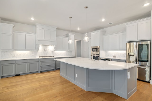 kitchen with appliances with stainless steel finishes, pendant lighting, white cabinets, and an island with sink