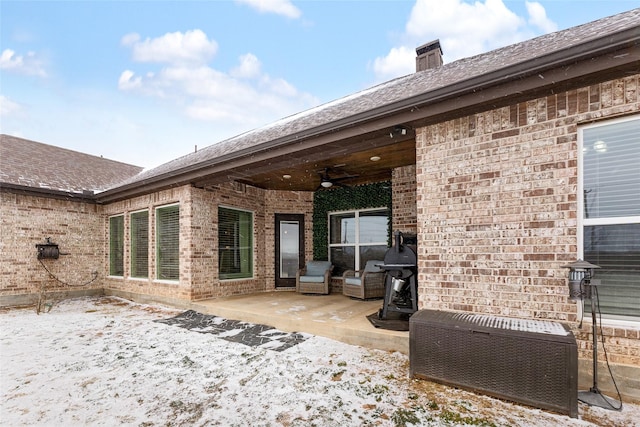 snow covered property with a patio area, a chimney, a ceiling fan, and brick siding