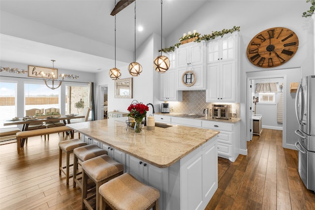 kitchen with hanging light fixtures, freestanding refrigerator, white cabinets, a kitchen island, and a sink