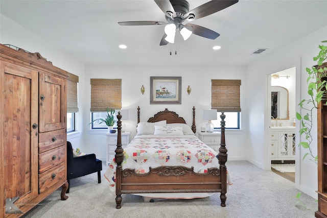 bedroom with baseboards, visible vents, light colored carpet, ensuite bath, and a sink