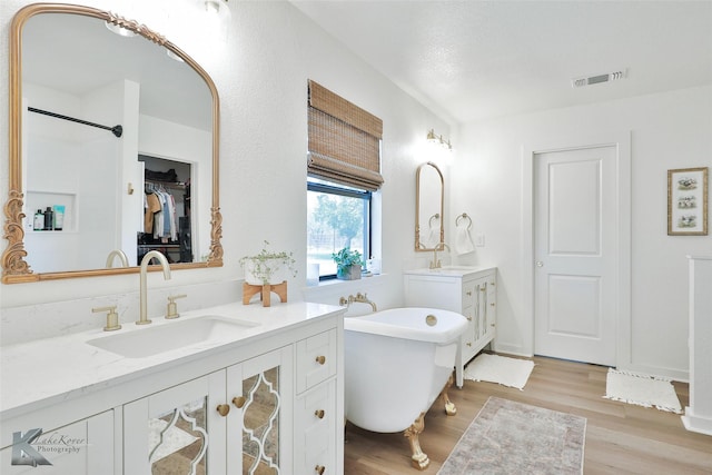 full bath with two vanities, visible vents, a spacious closet, a sink, and wood finished floors