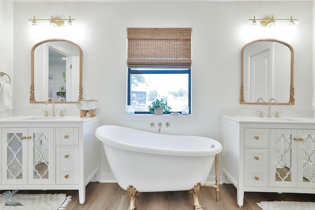 bathroom with a freestanding bath, wood finished floors, two vanities, and a sink