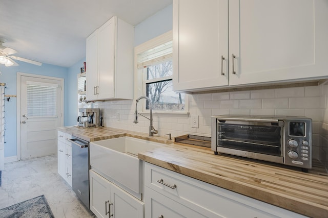 kitchen with marble finish floor, decorative backsplash, stainless steel dishwasher, a sink, and wood counters