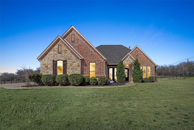 view of front of house featuring stone siding, roof with shingles, fence, a front yard, and brick siding