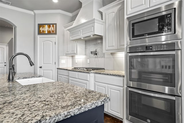 kitchen with appliances with stainless steel finishes, a sink, arched walkways, premium range hood, and visible vents