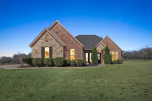 view of front of house featuring brick siding, stone siding, a front yard, and roof with shingles