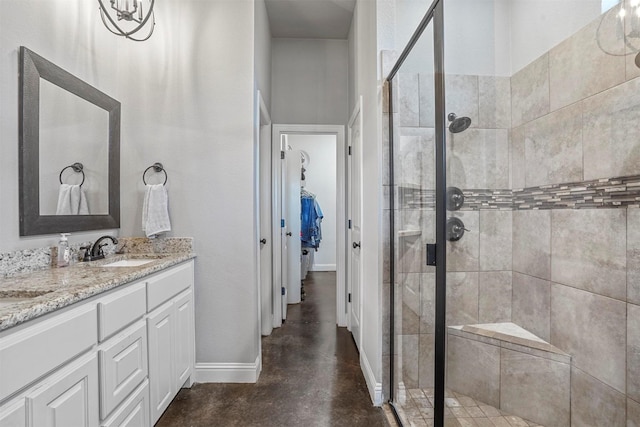 bathroom with double vanity, baseboards, a spacious closet, a shower stall, and a sink