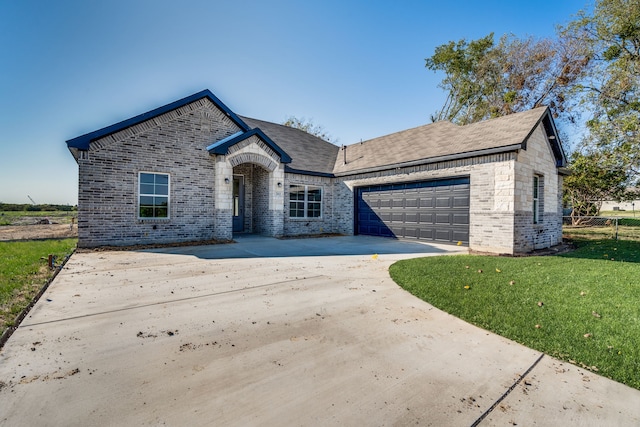 french country home featuring a garage, driveway, a front lawn, and brick siding