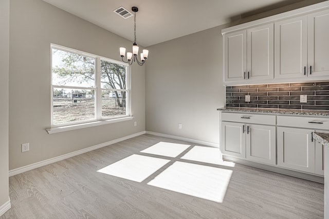 unfurnished dining area with an inviting chandelier, light wood-style flooring, visible vents, and baseboards