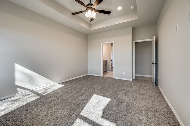 unfurnished bedroom with a raised ceiling, light colored carpet, a ceiling fan, ensuite bath, and baseboards