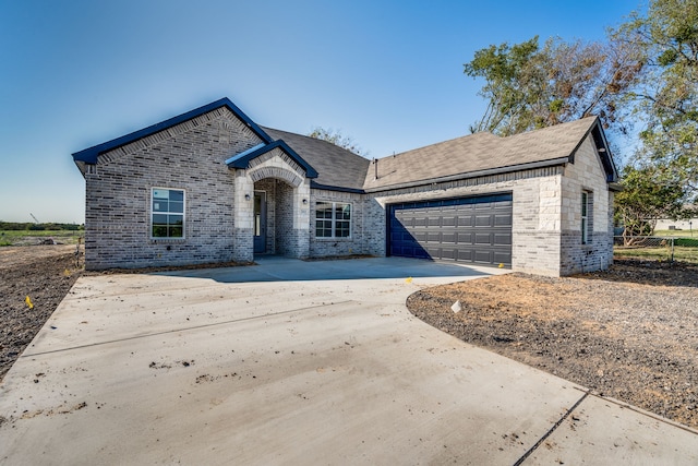 french country home with concrete driveway, brick siding, and an attached garage