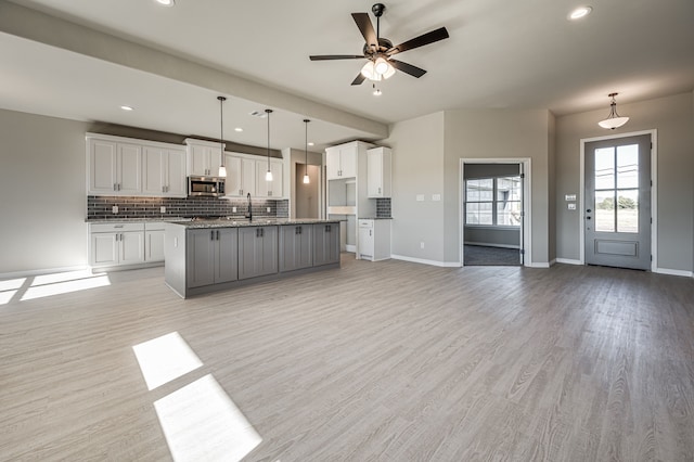 kitchen with open floor plan, stainless steel microwave, a center island with sink, and white cabinets