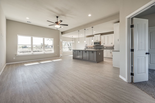 unfurnished living room featuring light wood-type flooring, a sink, baseboards, and ceiling fan with notable chandelier