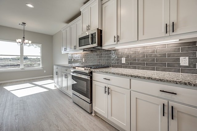 kitchen with decorative backsplash, appliances with stainless steel finishes, white cabinetry, light stone countertops, and light wood-type flooring