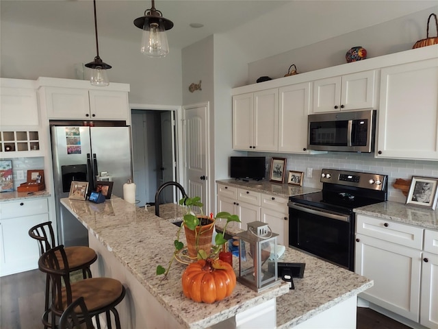 kitchen with a center island with sink, white cabinets, hanging light fixtures, stainless steel appliances, and backsplash