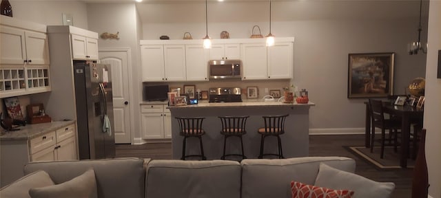 kitchen featuring baseboards, dark wood finished floors, appliances with stainless steel finishes, light stone counters, and pendant lighting