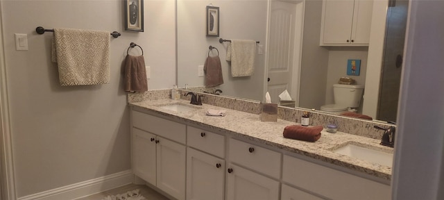 full bathroom with double vanity, a sink, toilet, and baseboards