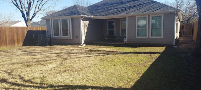 rear view of house featuring a yard, roof with shingles, and fence