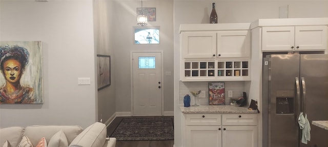 kitchen with hanging light fixtures, light stone countertops, stainless steel fridge, and white cabinets