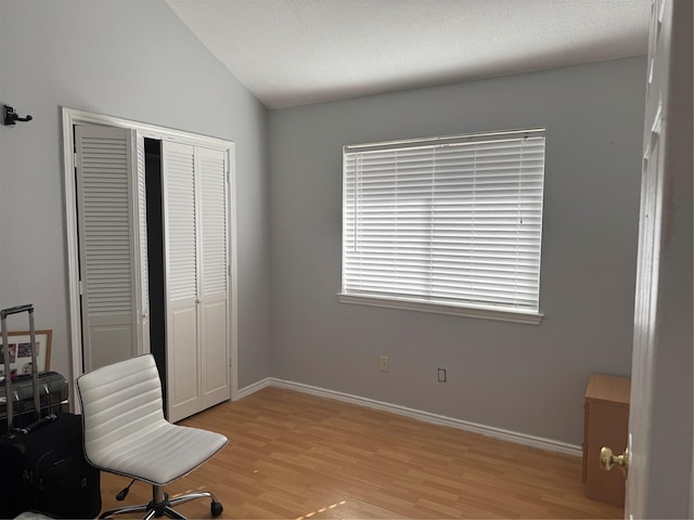 interior space with light wood-type flooring, a closet, lofted ceiling, and baseboards