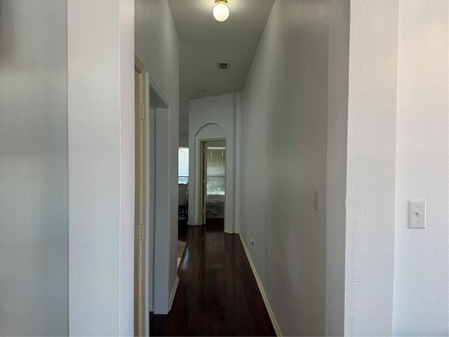 hallway featuring visible vents, baseboards, and dark wood-style flooring