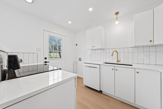 kitchen featuring white dishwasher, a sink, white cabinetry, light wood-style floors, and tasteful backsplash