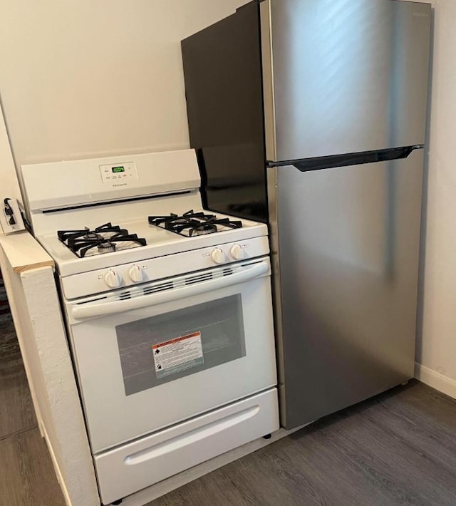 kitchen featuring baseboards, light countertops, freestanding refrigerator, white gas range, and dark wood finished floors