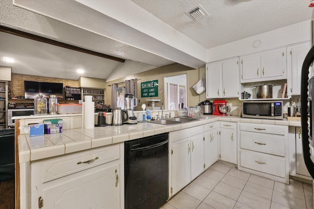 kitchen featuring tile counters, stainless steel microwave, a sink, dishwasher, and a peninsula